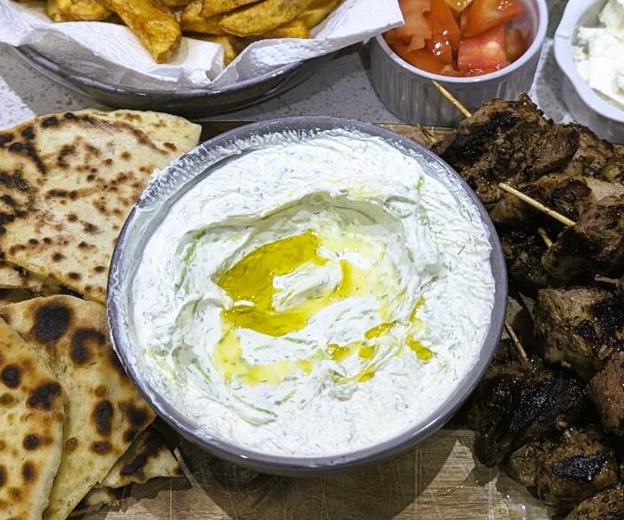 Tzatziki dip along with pita bread, meat, hot chips and salad